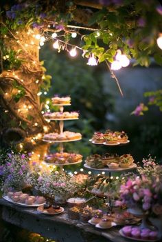 a table filled with cakes and cupcakes under a tree covered in fairy lights