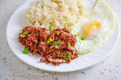 a white plate topped with rice and meat next to an egg on top of it