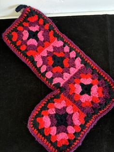 two crocheted items are sitting on the floor next to each other and one is pink, black, and red