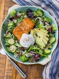 a bowl filled with salad and salmon on top of a wooden table