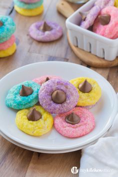 colorful doughnuts with chocolate on them sitting on a white plate next to other pastries