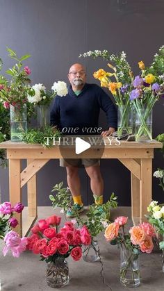 a man sitting at a table surrounded by vases filled with flowers and greenery