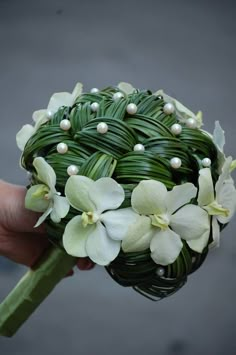 a bouquet made out of wicker with white flowers and pearls on the stems is held by a person's hand