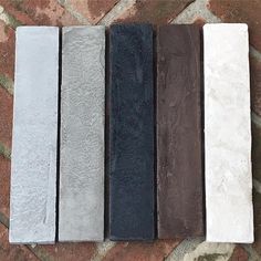 four different colors of tile laid out on a brick floor with one black, the other white