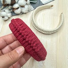 a hand holding a piece of red yarn next to cotton balls and a string on a table