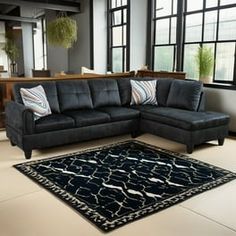 a living room with a black sectional couch and rug in front of large open windows