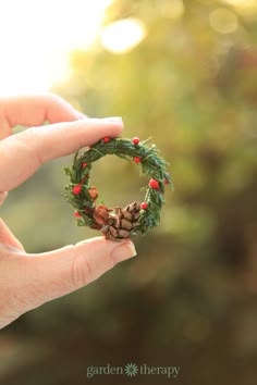 a hand holding a miniature wreath with pine cones and berries