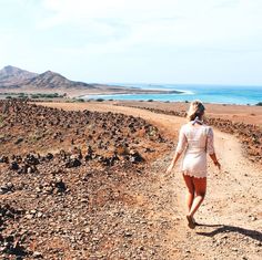 a woman walking down a dirt road next to the ocean