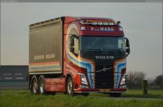 a red volvo semi truck driving down a road next to a grass covered parking lot