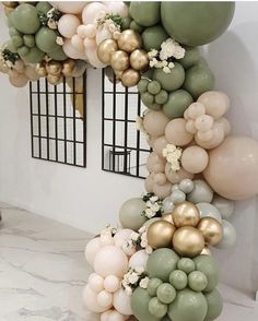 the balloon arch is decorated with gold and white balloons, greenery and flowers on it