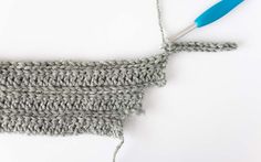 the crochet stitch is being worked on with a blue handled knitting needle in front of it