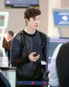 a young man with ear buds is looking at his cell phone in an airport terminal