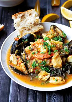 a white plate topped with clams and mussels next to slices of lemon