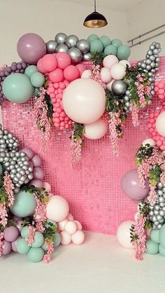 balloons and garlands are hanging from the ceiling in front of a pink backdrop with silver, white, and pink balls