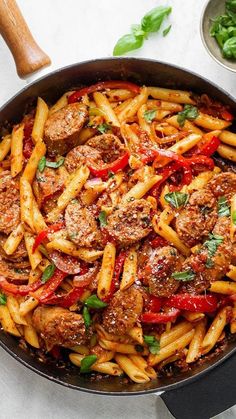 a skillet filled with pasta and meat covered in marinara sauce, garnished with fresh basil