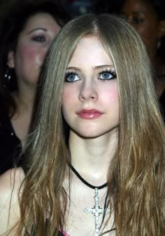 a woman with long blonde hair and blue eyes is looking at the camera while wearing a cross necklace