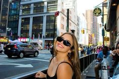 a woman standing on the side of a street next to tall buildings with people walking by