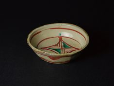 a white bowl with red and green designs on the inside is sitting on a black surface