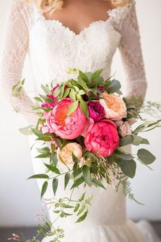 a woman holding a bouquet of flowers in her hands and wearing a wedding dress with lace sleeves