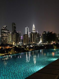 an empty swimming pool in front of a cityscape at night with lights reflecting off the water