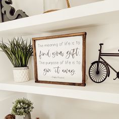 a white shelf with a wooden sign and potted plants on it, along with a bicycle