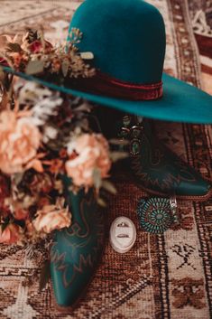 a blue cowboy hat and some flowers on a rug next to a pair of boots