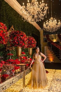 a woman in a dress standing next to a table with flowers and chandeliers