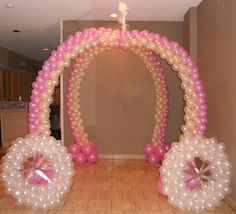 an arch made out of balloons with pink bows and pearls on the bottom, along with other decorations