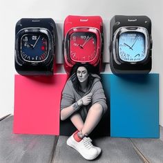 a woman sitting in front of four different colored clocks