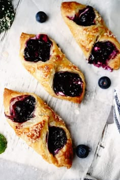 three pastries with blueberries and mint on a white tablecloth next to some flowers