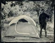 a man standing next to a tent in the woods