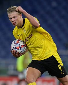 a soccer player holding a ball in his right hand and looking down at the ground