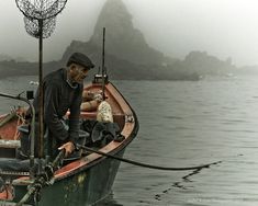 a man standing on top of a boat in the water next to another person wearing a hat