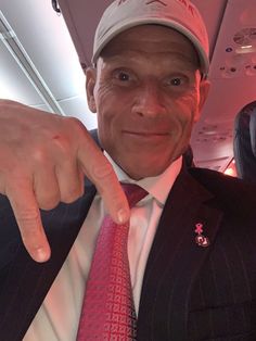 a man in a suit and tie points at the camera while on an air plane