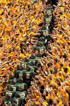 a large group of people in green and yellow uniforms with their hands up to the sky