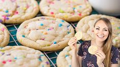 a woman holding up a cookie next to a rack full of sprinkles