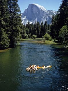 two people are floating on a raft in the middle of a river with mountains in the background