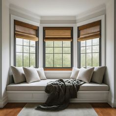 a white window seat with pillows and blankets on it in front of two large windows