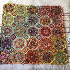 an old quilt is laying on a bed with white sheets and colorful flowers in the center