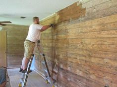 a man on a ladder painting the walls in a room with wood paneling and ceiling fans