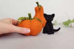 a hand is holding an orange and black cat figurine next to each other