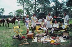 a group of people standing around a horse and carriage in the grass with horses behind them