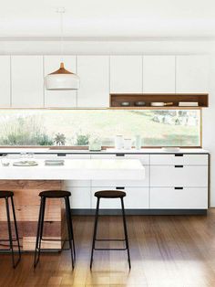 two stools sit in front of a kitchen island with white cabinets and counter tops