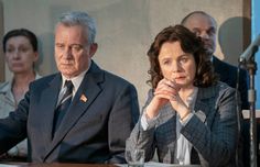 three people sitting at a table with microphones in front of them and one person holding his hand to his chin