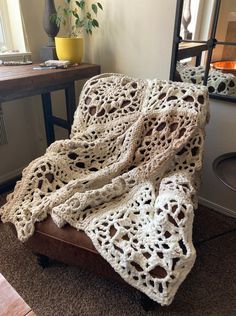 a crocheted blanket sitting on top of a wooden chair next to a table