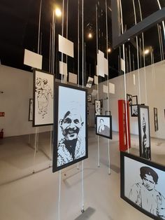 an art gallery with paintings hanging from the ceiling and framed pictures on display in front of them