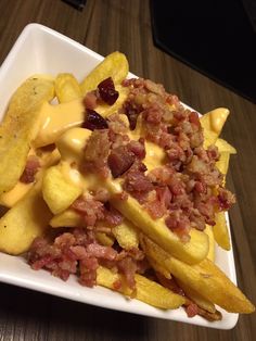 a white plate topped with french fries covered in cheese and bacon next to potato wedges