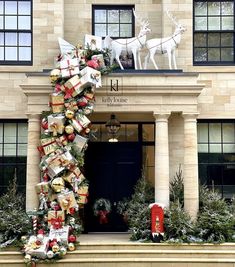 a large christmas tree with presents on it in front of a building that is decorated for the holiday season