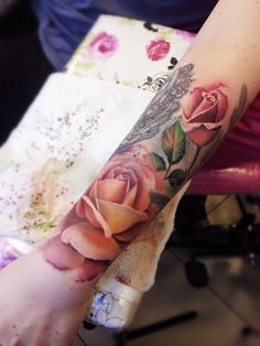 a woman's arm with roses and a bird tattoo on her left arm, while sitting in a chair