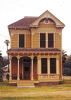 an old yellow house sitting on top of a lush green field in front of a palm tree